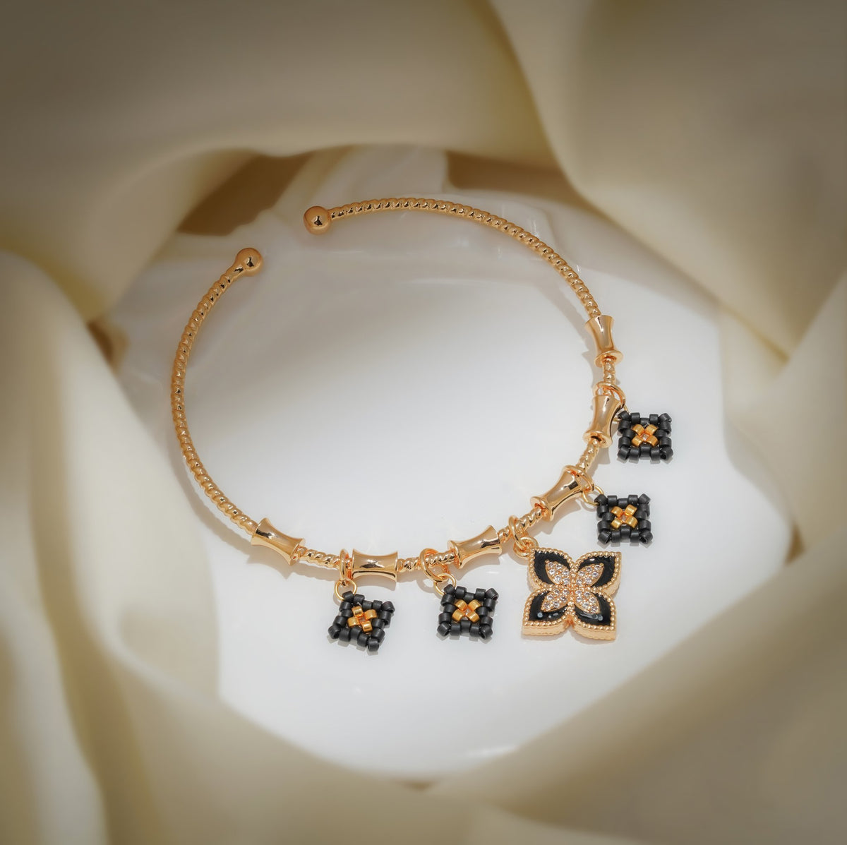 Gold open bangle with black beaded diamond charms and a crystal black clover charm on cream silk