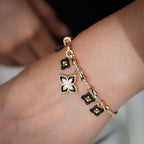 Gold charm bangle worn on the wrist, showing black beaded diamonds and the crystal clover charm
