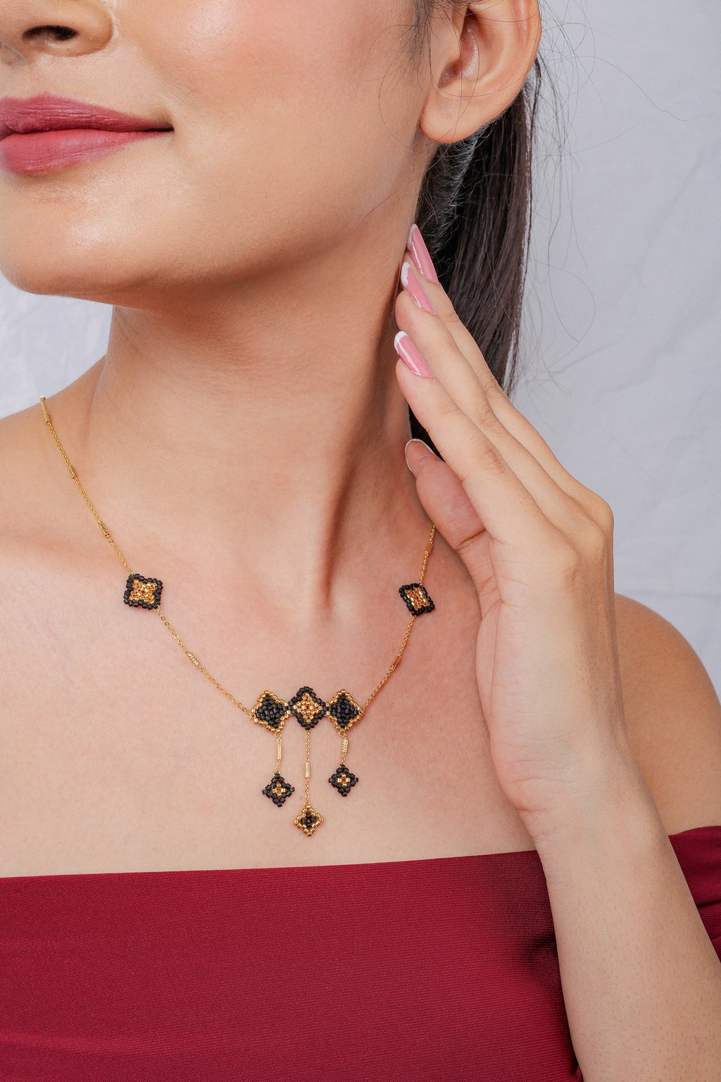 Gold chain necklace with black and gold beaded rhombus trio and three dangling drops, worn by model