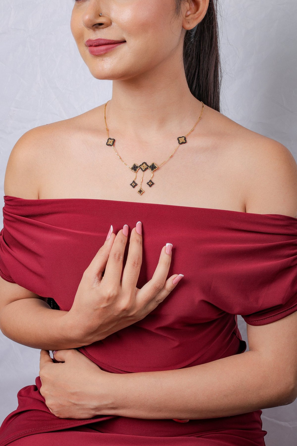 Model in off-shoulder top wearing black and gold beaded rhombus necklace