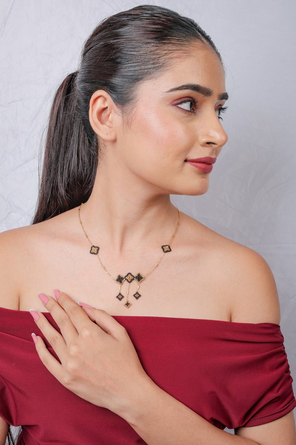 Model looking sideways, wearing gold chain with black beaded rhombus centrepiece