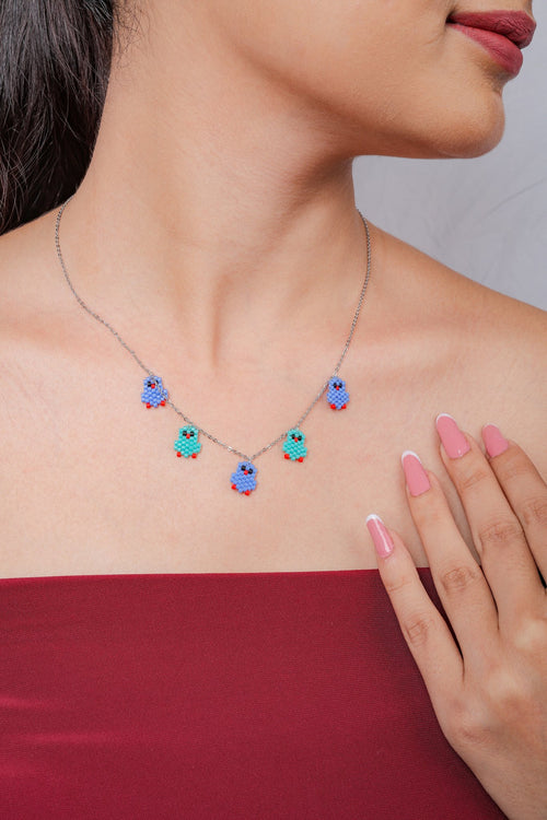 Silver chain necklace with five blue and turquoise beaded bird charms worn at the collarbone
