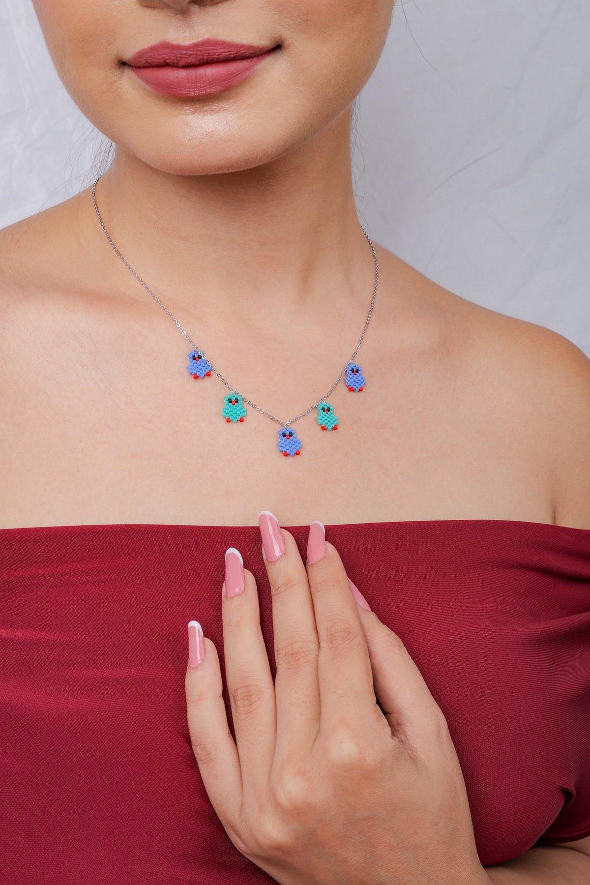 Model wearing the blue and turquoise beaded bird charm necklace with a red top
