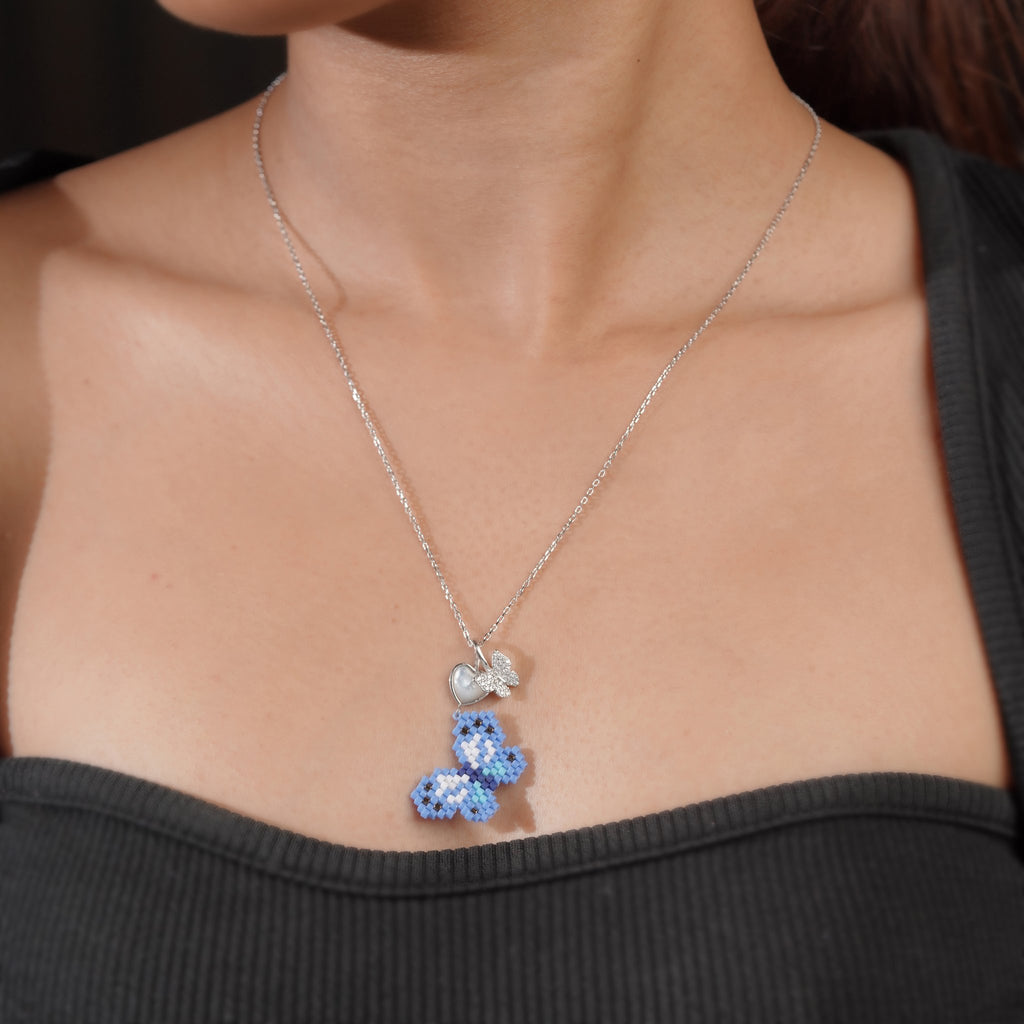 Model wearing silver necklace with blue beaded butterfly pendant against a black top