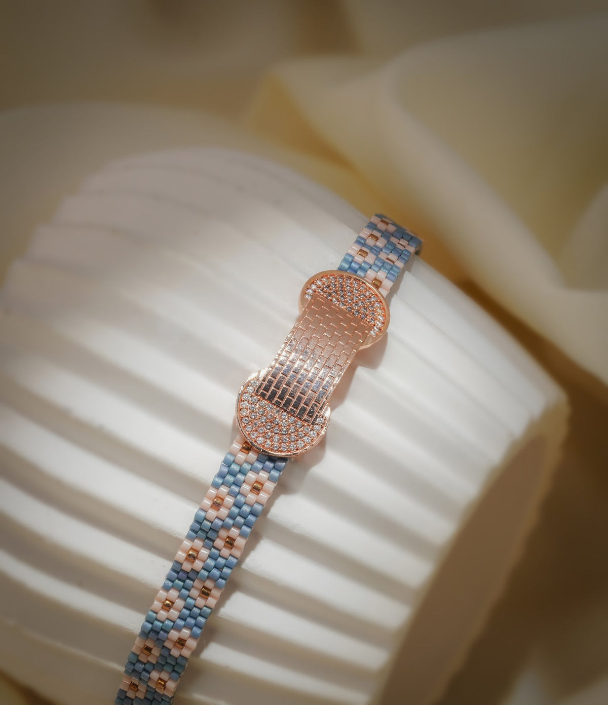 Blue daisy woven bead bracelet with rose-gold pavé centrepiece wrapped around a ribbed stand
