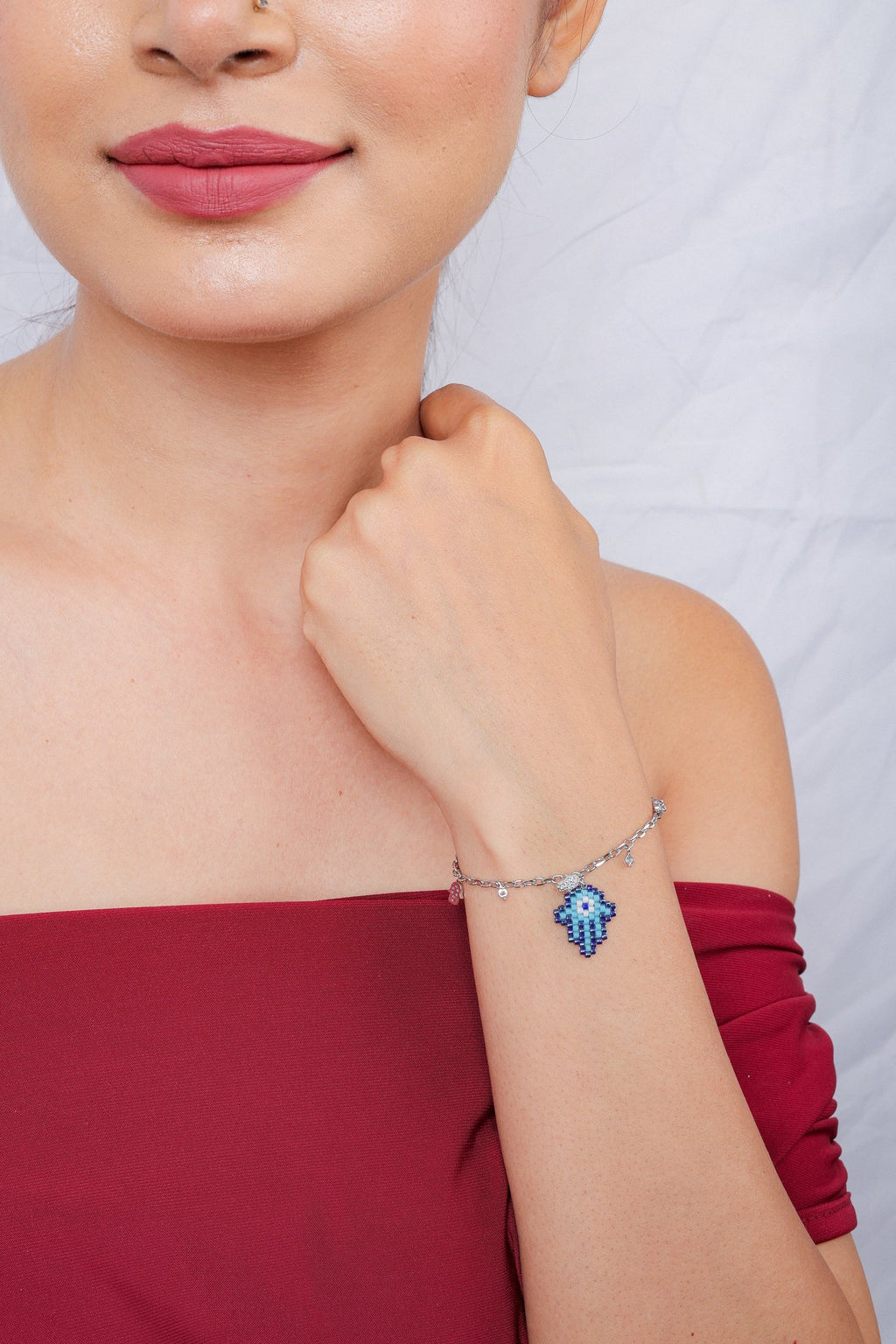 Model holding her wrist near her chin, showing a silver-tone bracelet with a blue hamsa