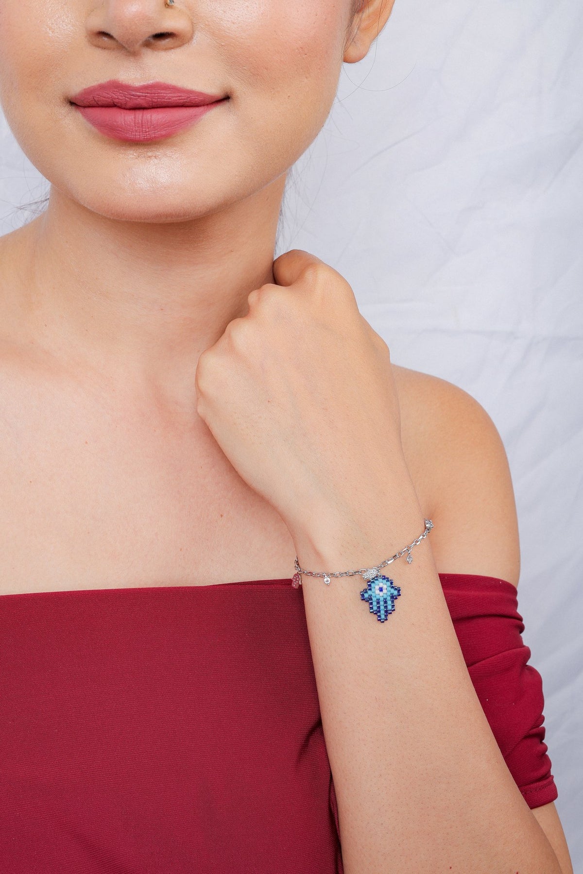 Model holding her wrist near her chin, showing a silver-tone bracelet with a blue hamsa