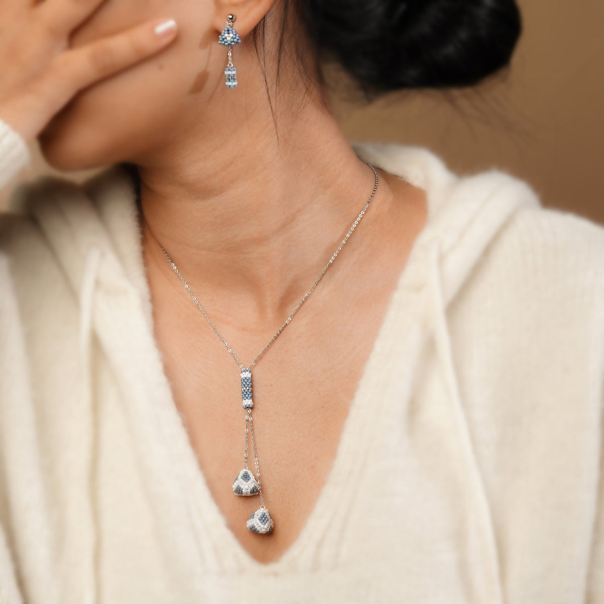 Model wearing powder-blue beaded lariat necklace and matching drop earrings with a cream knit