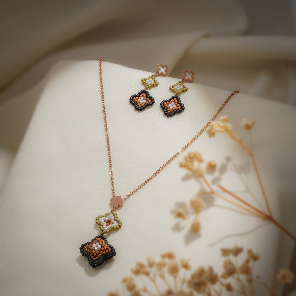 Rose-gold necklace with olive and bronze beaded clover drop and matching earrings on cream silk