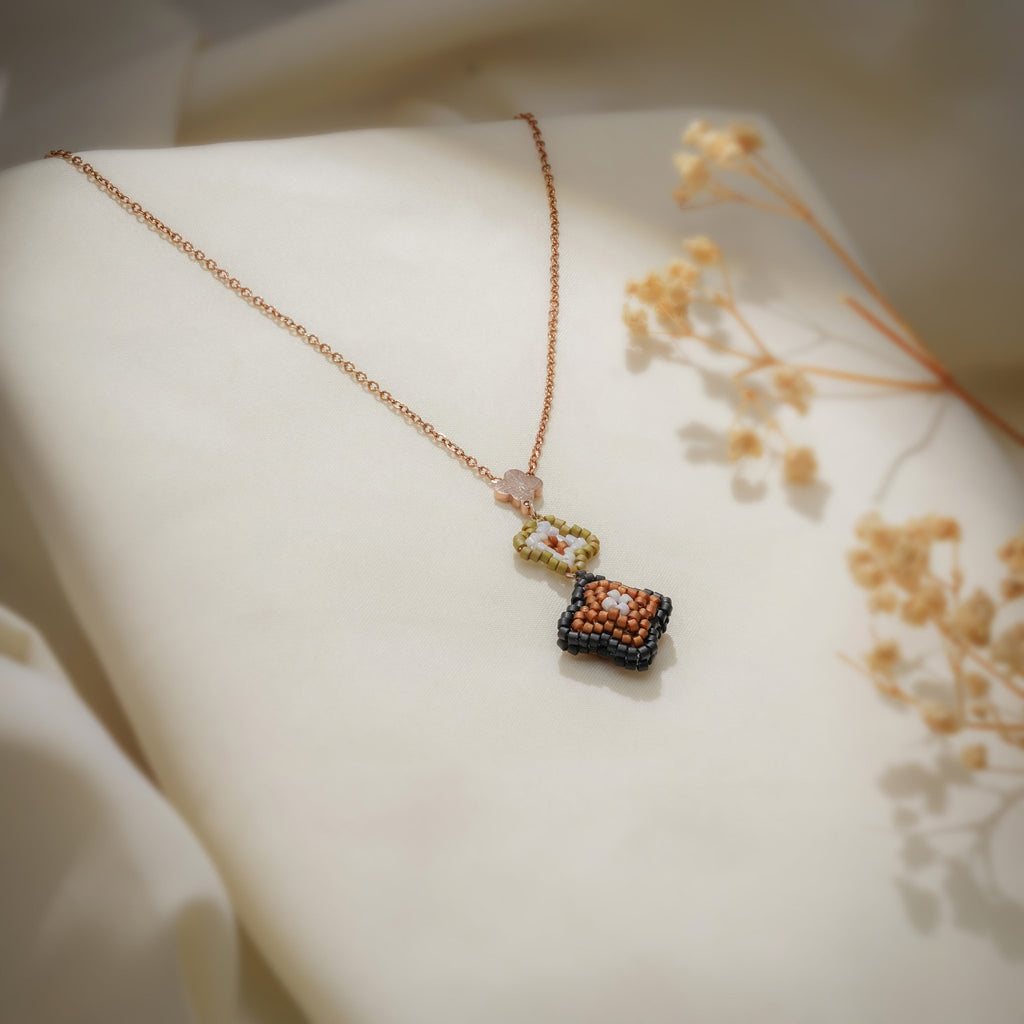 Bronze beaded clover pendant on a rose-gold chain draped over cream fabric