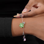 Hand holding the charm bracelet on the wrist, showing the green beaded flower and crystal charms