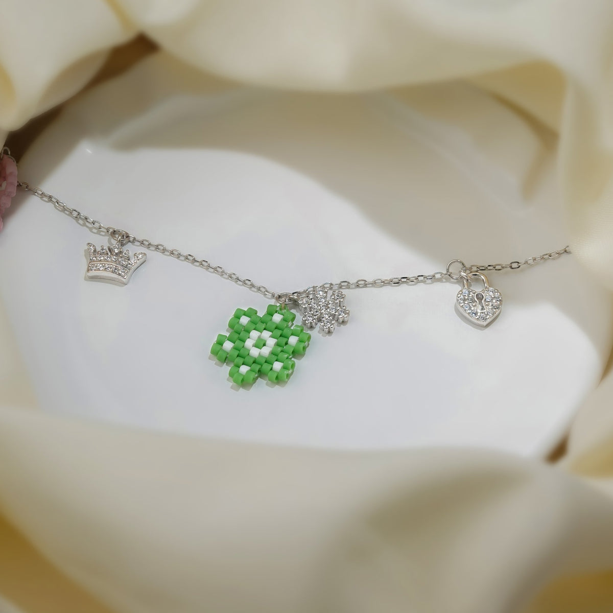 Green beaded flower, crystal crown and heart padlock charms on a silver chain bracelet
