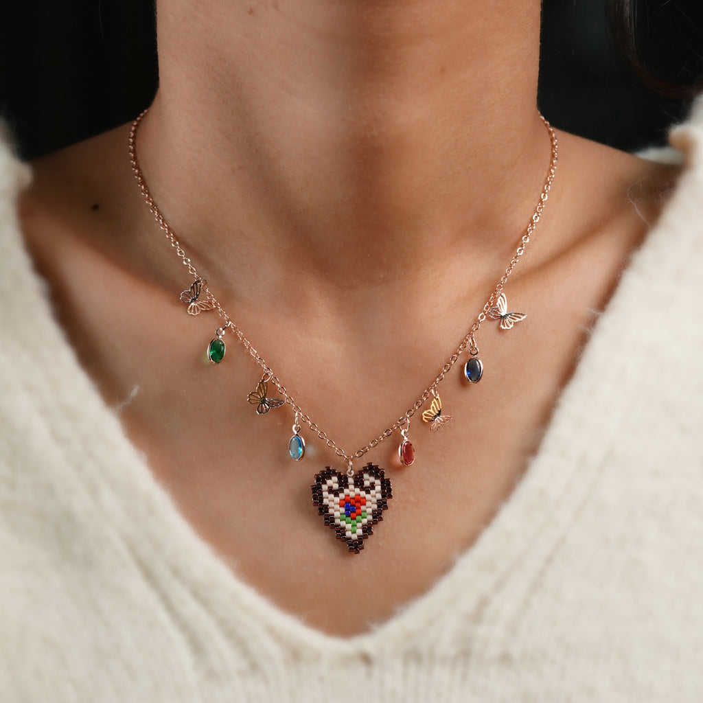 Model wearing rose-gold butterfly charm necklace with beaded heart pendant over a white knit