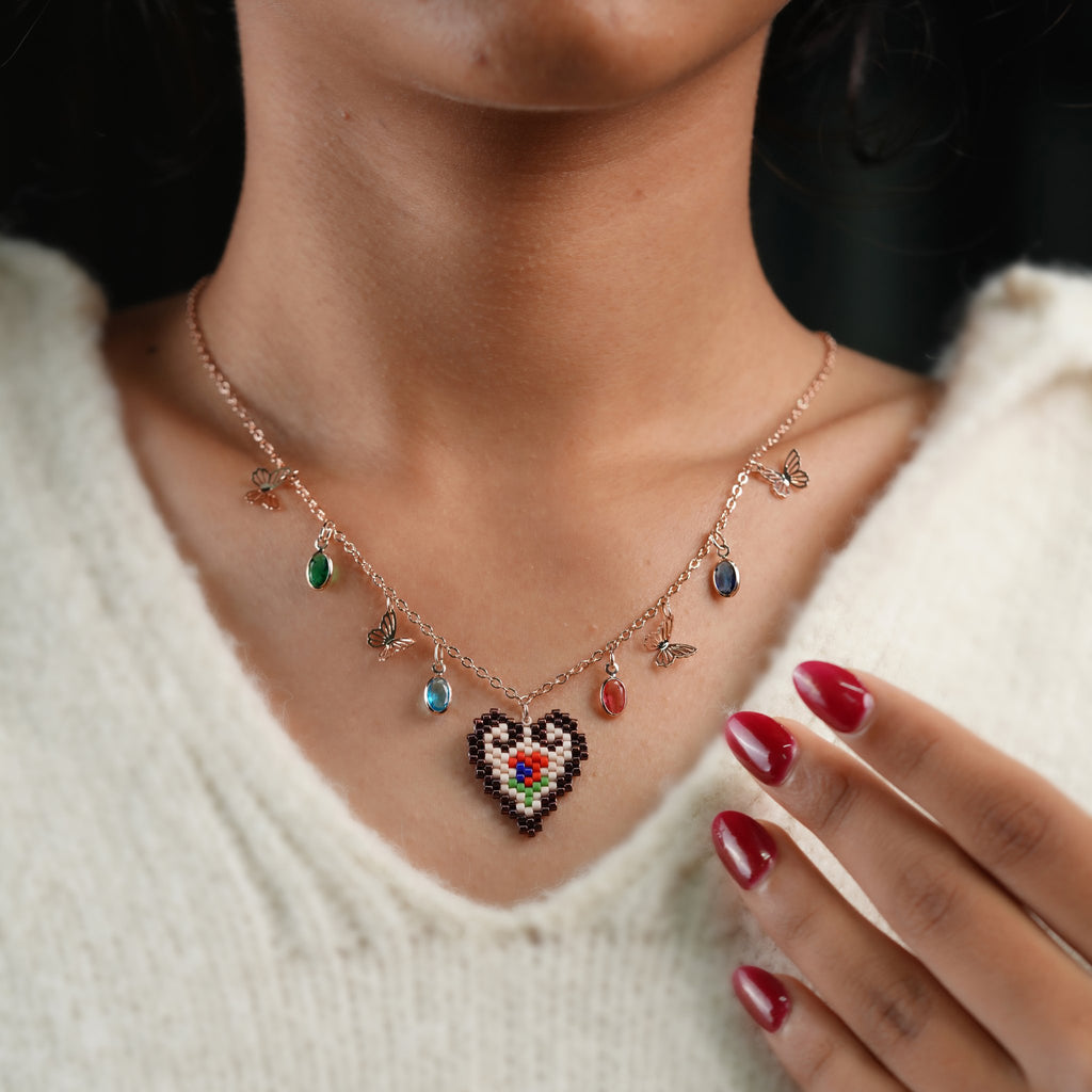 Model touching collarbone, wearing heart pendant necklace with butterflies and colourful crystals