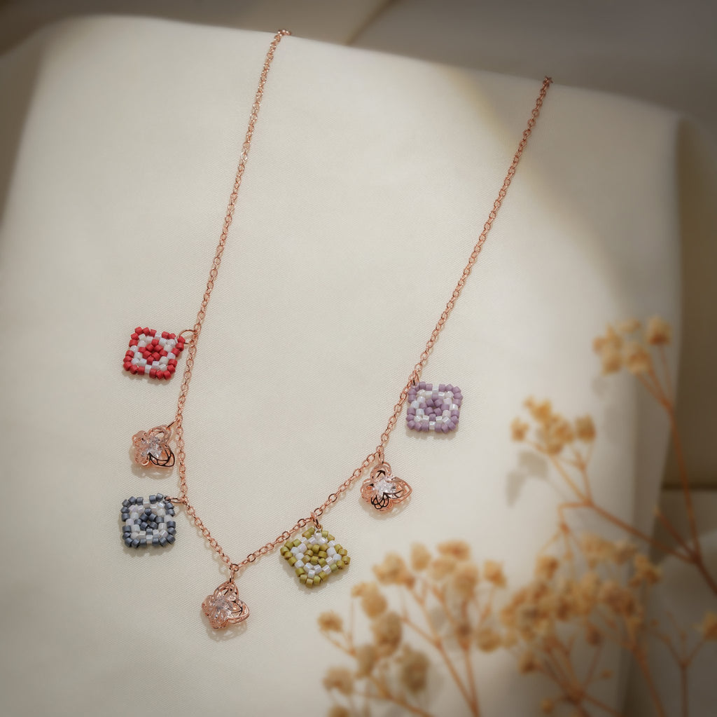 Rose-gold charm necklace with red, lilac, grey and olive beaded squares and filigree butterflies on cream silk