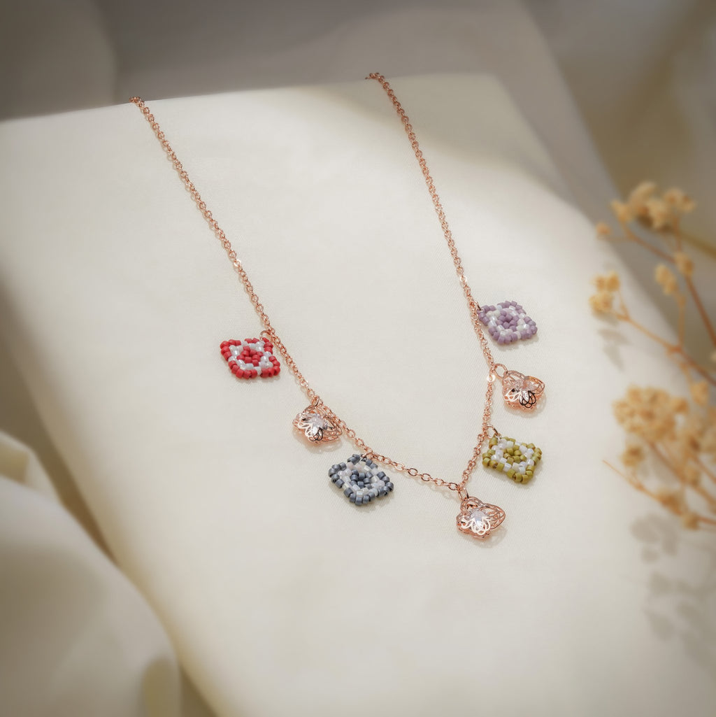 Beaded square and crystal butterfly charm necklace draped over cream fabric with dried flowers