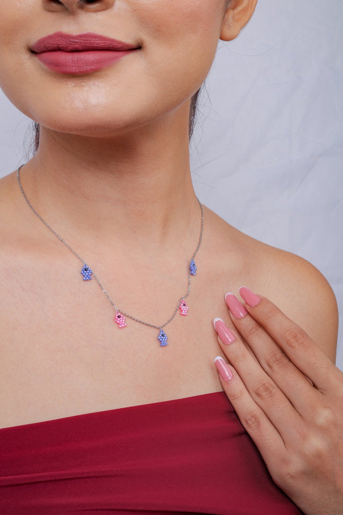 Fish charm necklace shown at an angle on a model, hand resting on her shoulder
