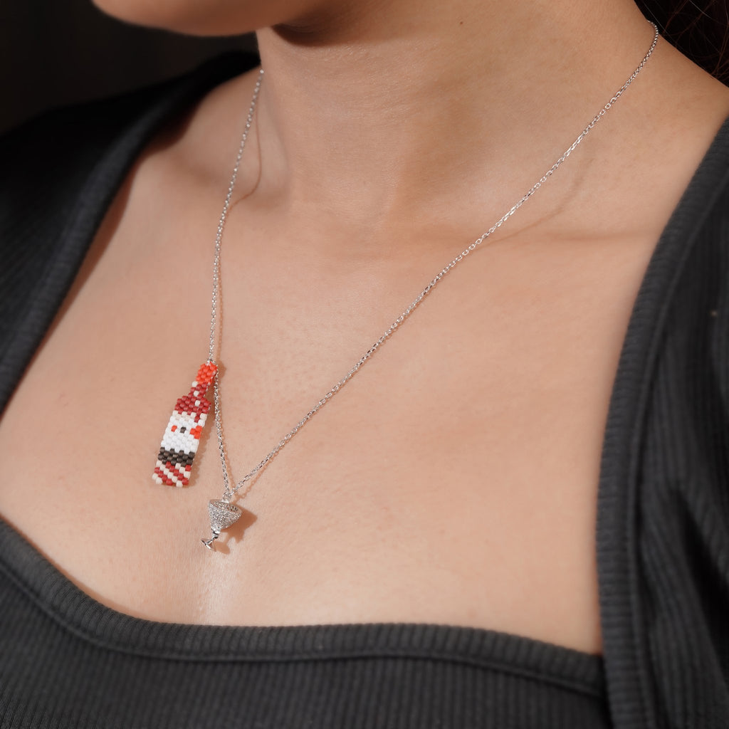 Model wearing the beaded bottle and crystal glass charm necklace over a black top