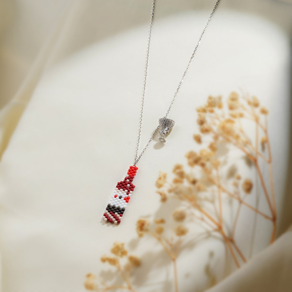 Beaded bottle and crystal cocktail glass charms on a silver chain over cream fabric
