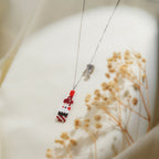 Beaded bottle and crystal cocktail glass charms on a silver chain over cream fabric