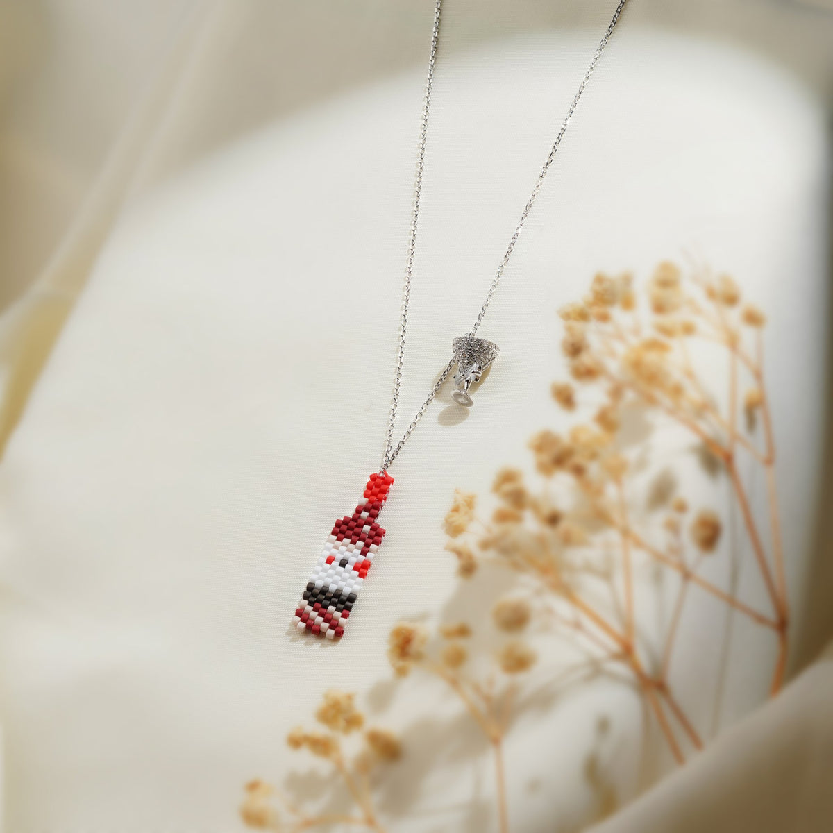 Beaded bottle and crystal cocktail glass charms on a silver chain over cream fabric