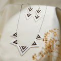 Silver chain necklace with five white and brown chevron triangle charms beside matching earrings