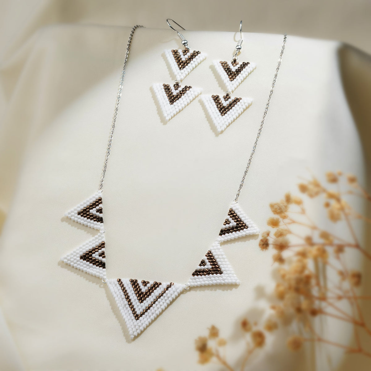 Silver chain necklace with five white and brown chevron triangle charms beside matching earrings