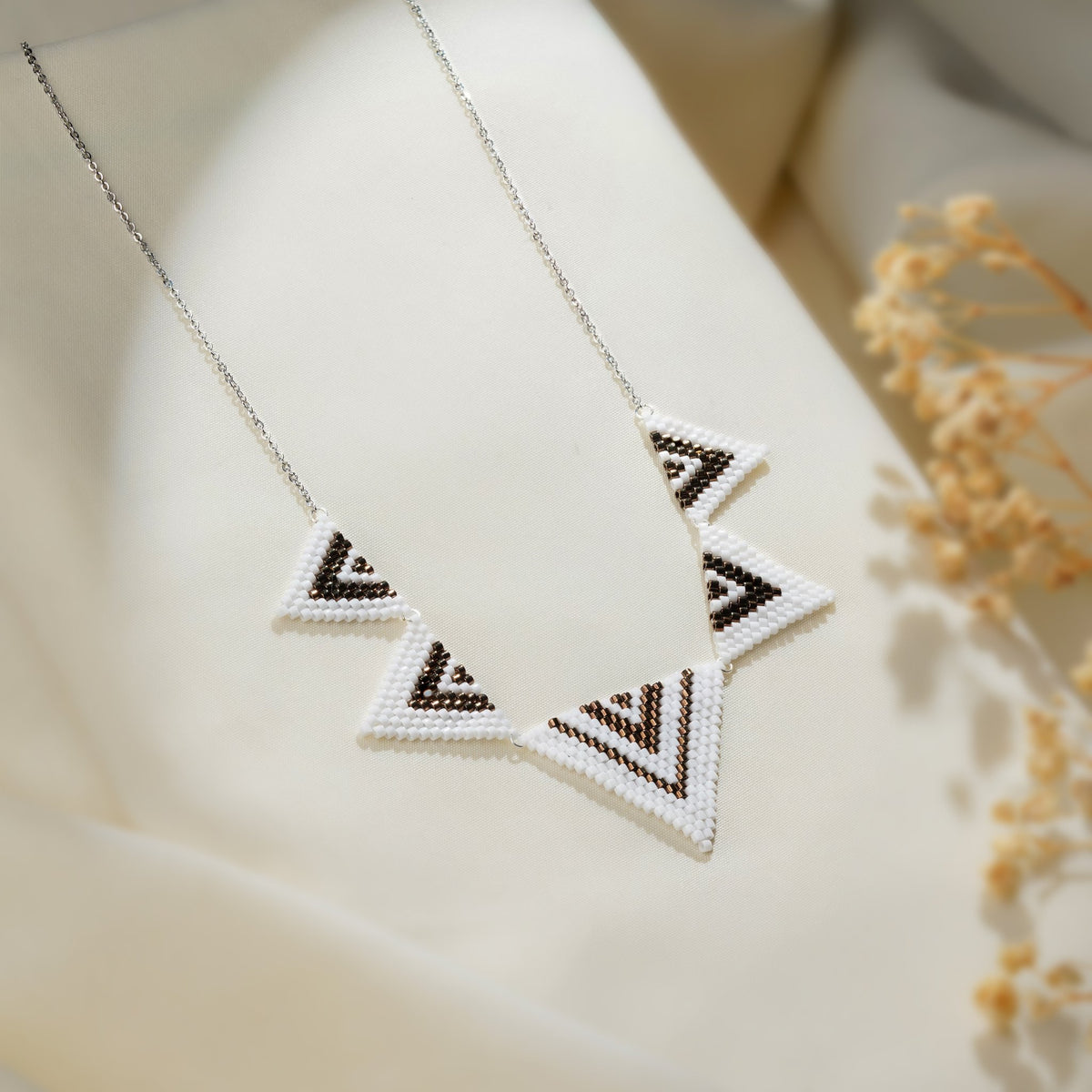 Silver chain necklace with five beaded white triangles striped in brown chevrons on cream fabric