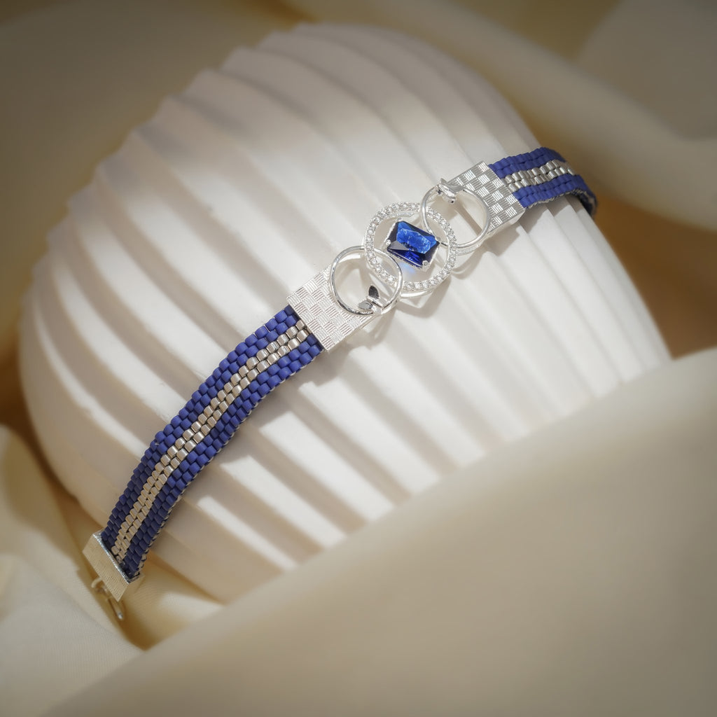 Cobalt loom bracelet draped over a ribbed white stand, showing the silver stripe and clasp end