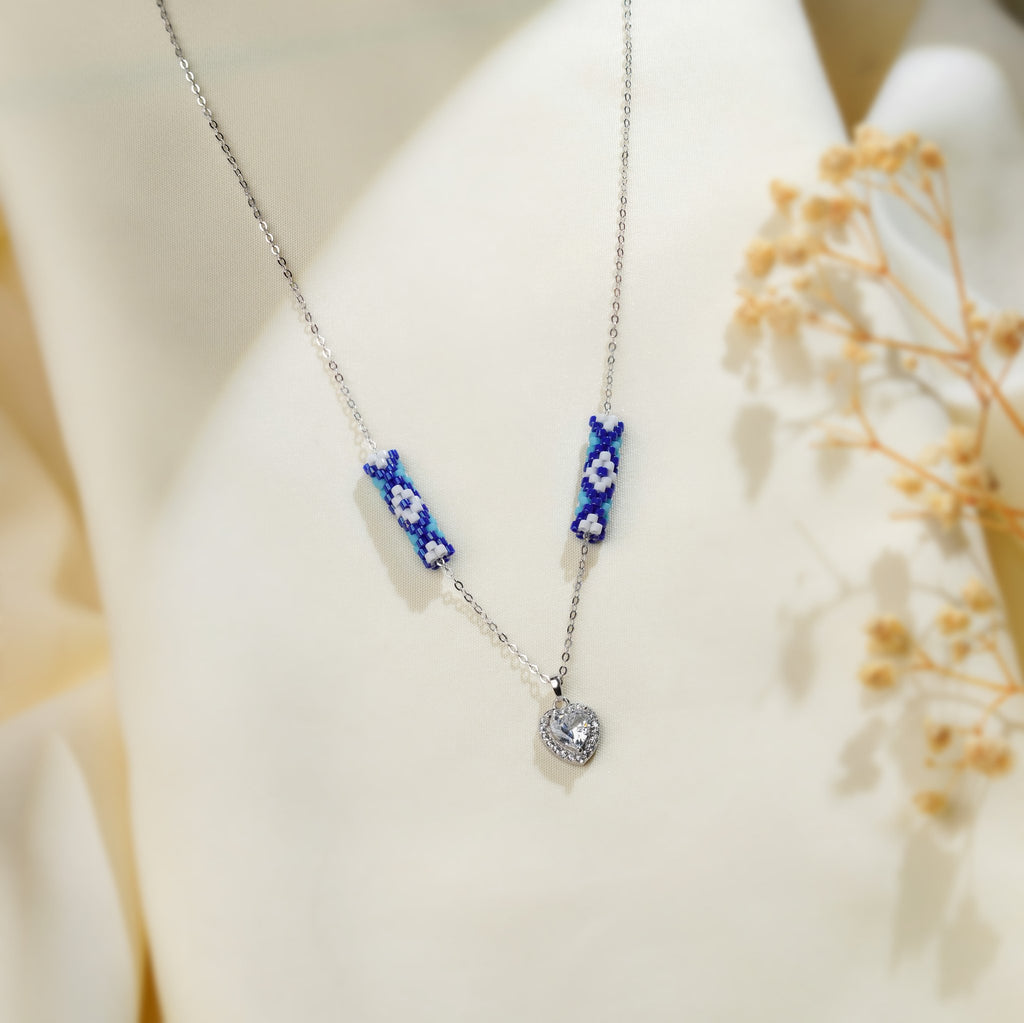 Silver chain necklace with two cobalt daisy-beaded tubes and a crystal halo heart pendant on cream silk