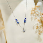 Silver chain necklace with two cobalt daisy-beaded tubes and a crystal halo heart pendant on cream silk