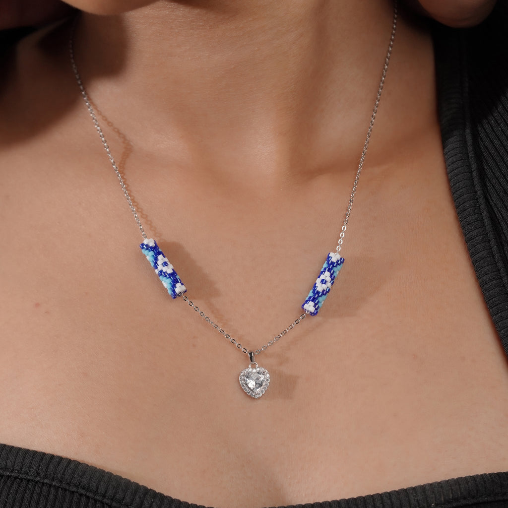 Model wearing silver necklace with cobalt beaded tubes and sparkling crystal heart pendant