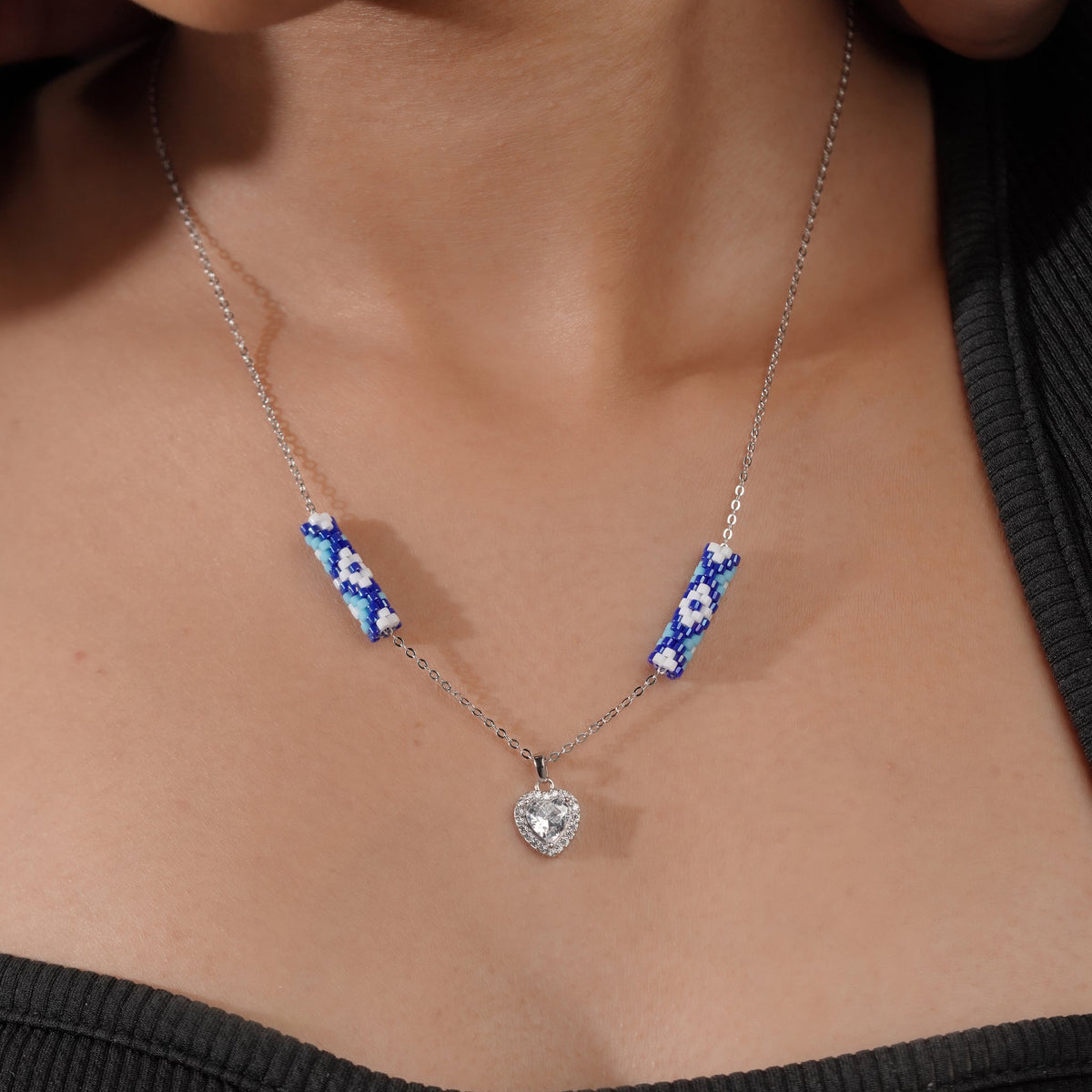 Model wearing silver necklace with cobalt beaded tubes and sparkling crystal heart pendant