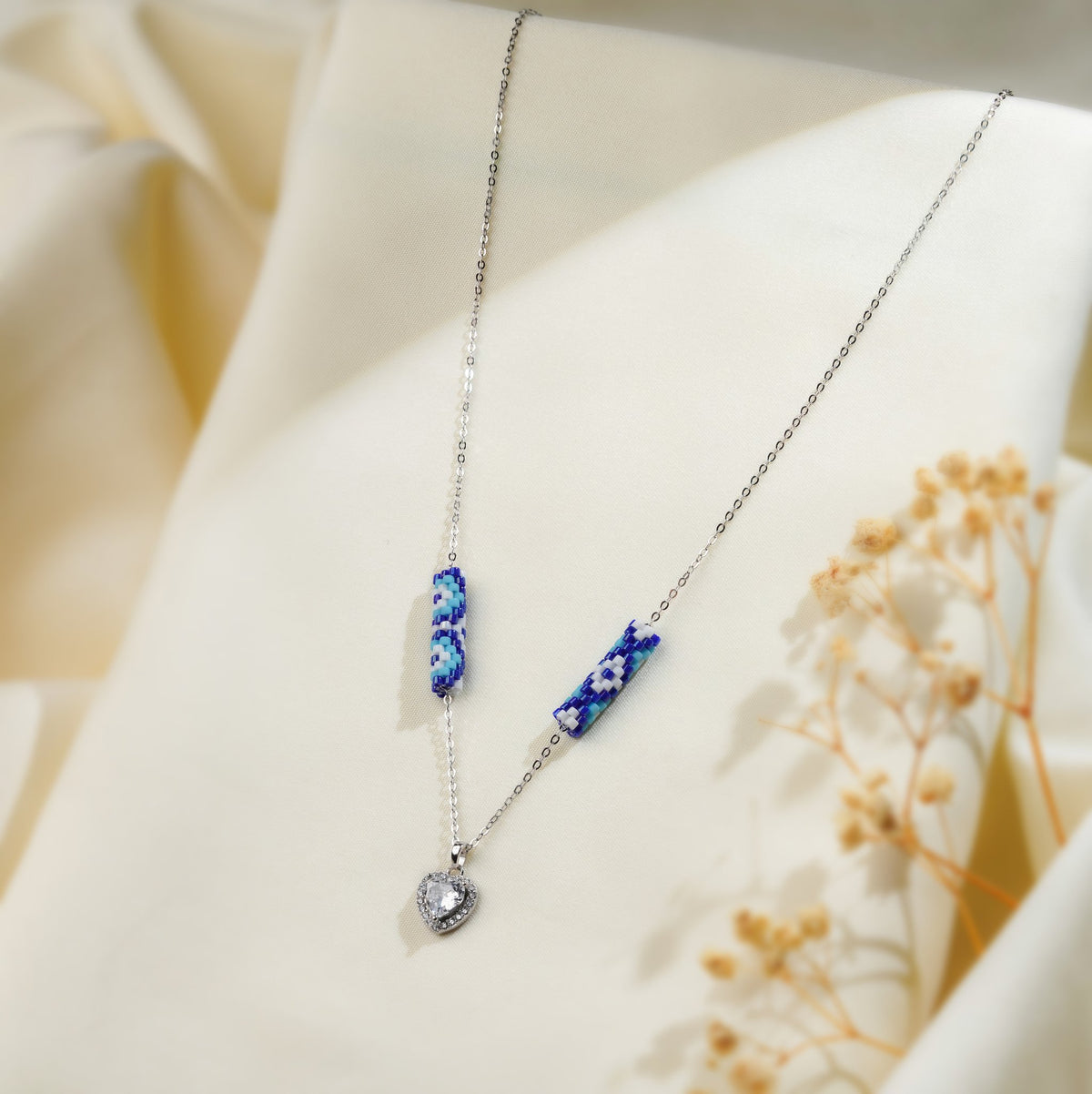 Angled view of cobalt and white daisy tube beads and crystal heart pendant on a fine silver chain