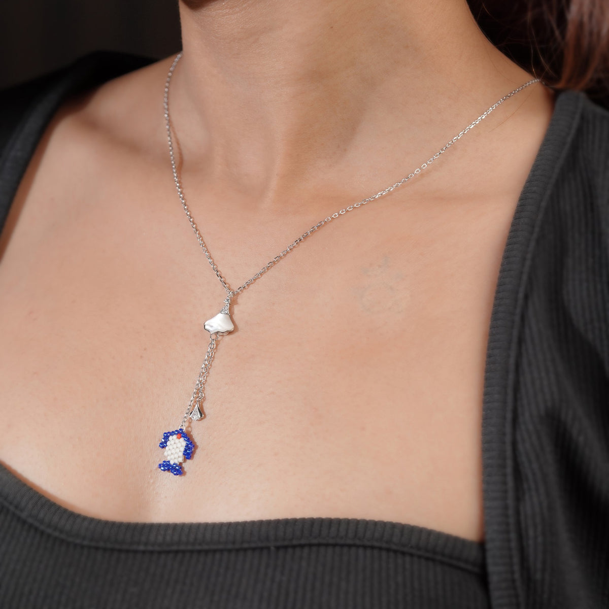 Model wearing silver Y-necklace with cobalt beaded charm and small crystal fan drop