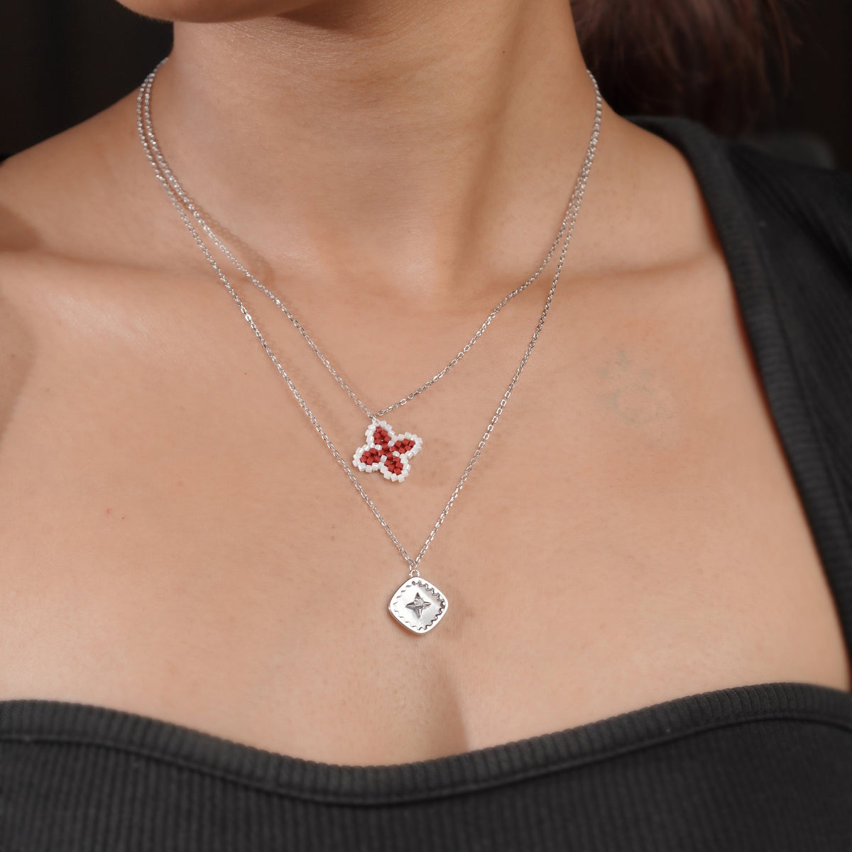 Model wearing a layered silver-tone necklace with red clover and star pendants