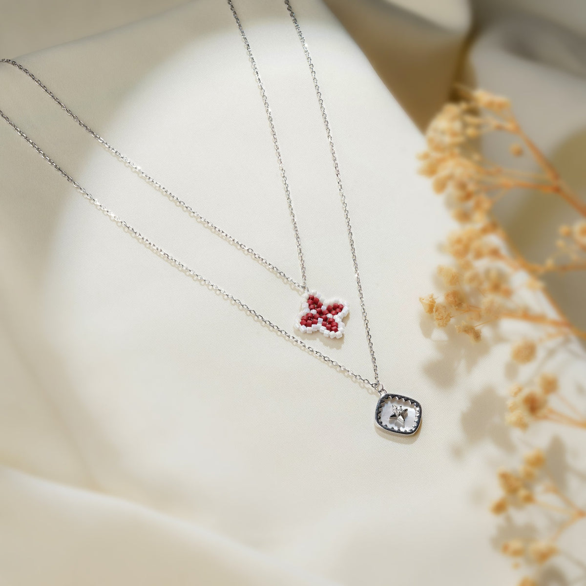 Layered necklace with red four-petal bead charm and star pendant on cream fabric