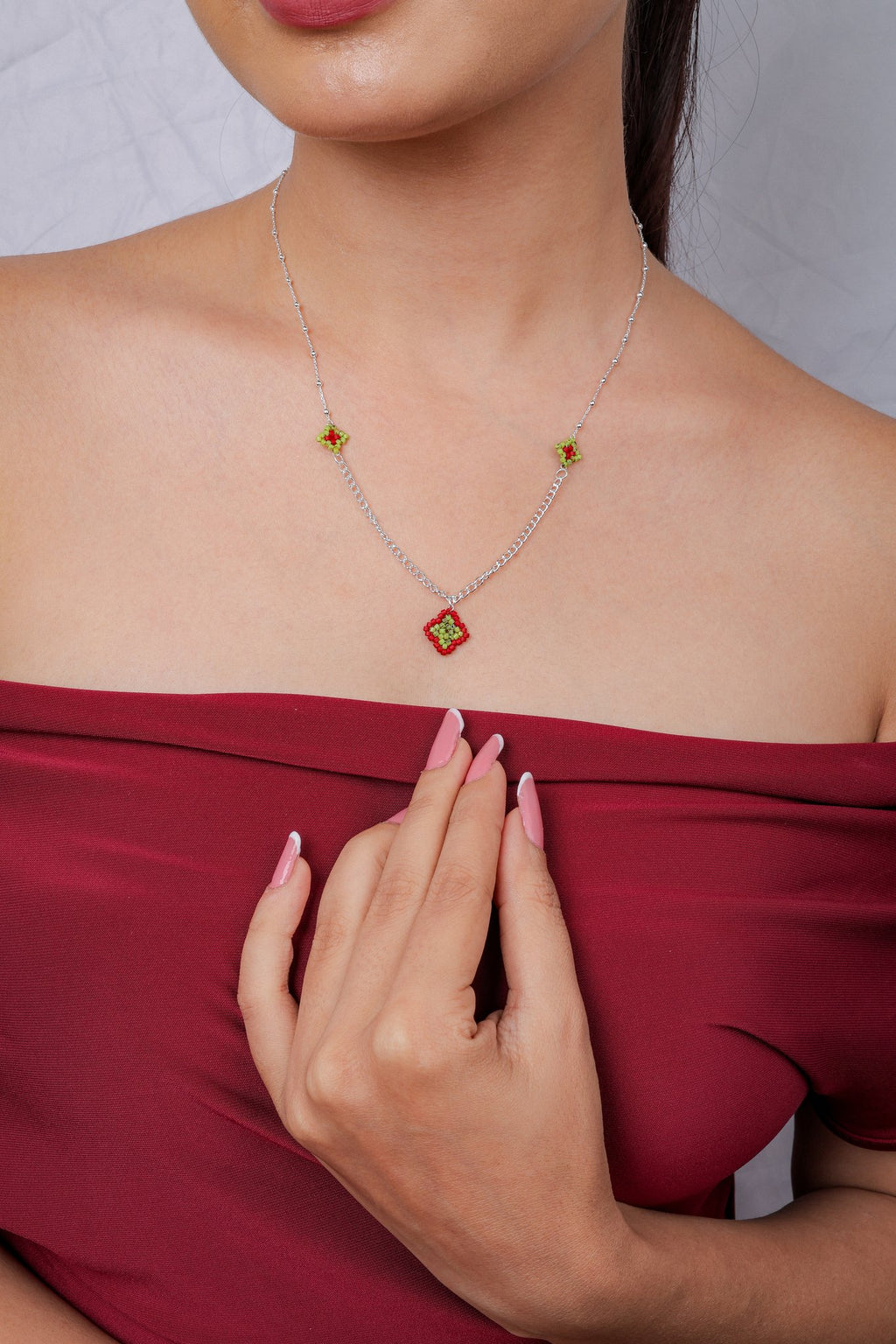 Red beaded diamond pendant necklace on a silver chain worn with a red off-shoulder top