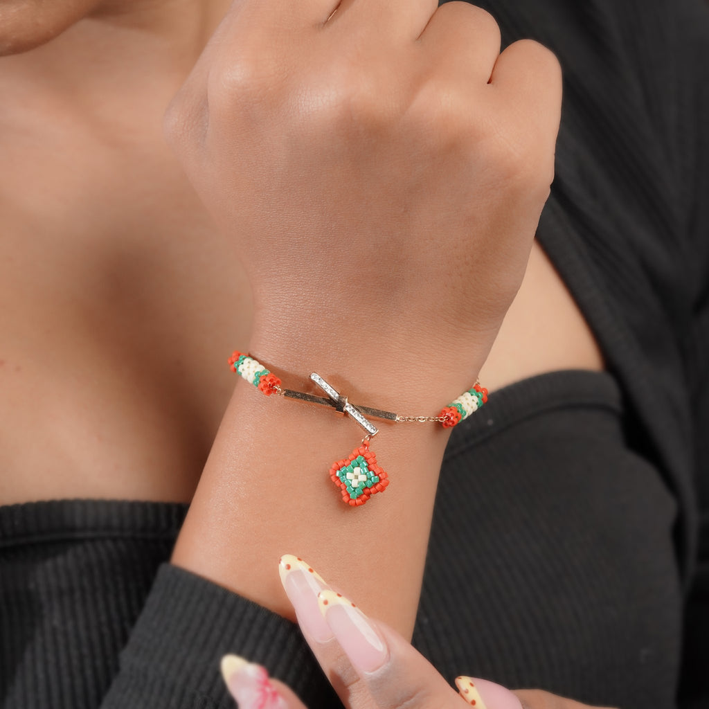 Rose-gold crossbar bracelet with red and green beaded diamond charm worn on the wrist