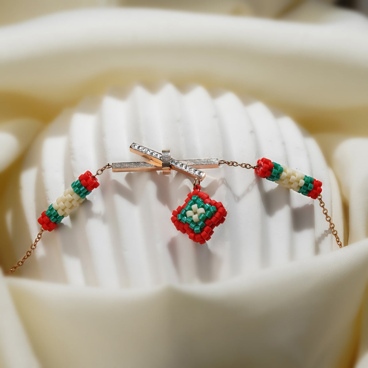 Red, green and cream beaded tubes and diamond charm on a rose-gold chain over a white stand