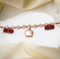 Rose-gold crystal-link bracelet with pearly white apple charm and two red beaded barrels on white