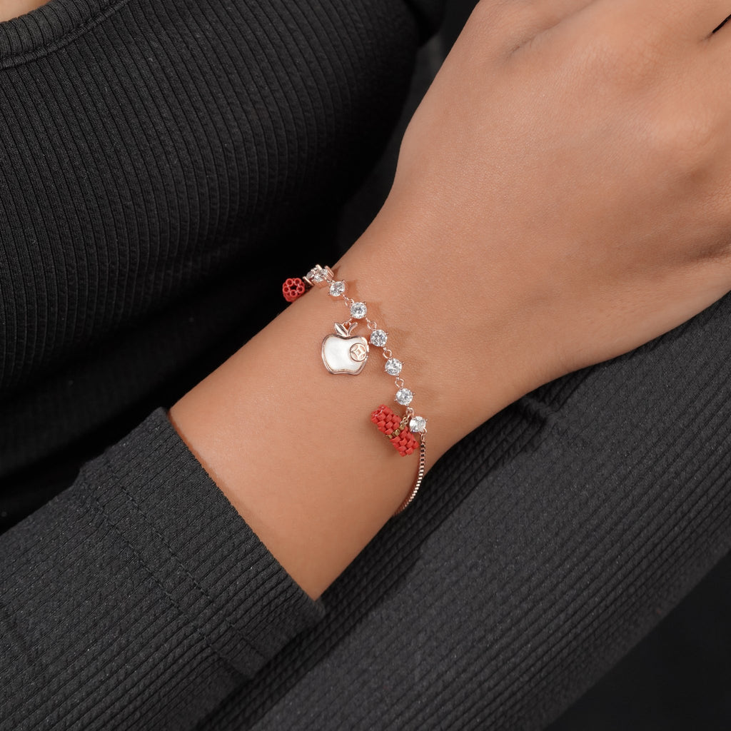 Rose-gold crystal apple charm bracelet worn on the wrist with red beaded barrel accents