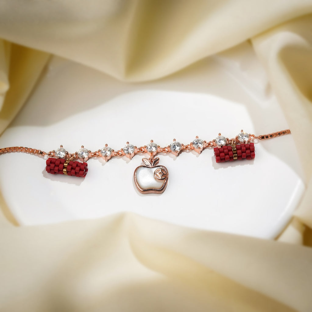 Rose-gold bracelet with crystal links, white apple charm and red beaded barrels on cream silk