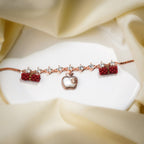 Rose-gold bracelet with crystal links, white apple charm and red beaded barrels on cream silk