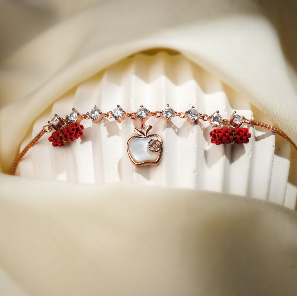 Crystal-link apple charm bracelet with red beaded barrels displayed on a ribbed white stand