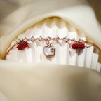 Crystal-link apple charm bracelet with red beaded barrels displayed on a ribbed white stand