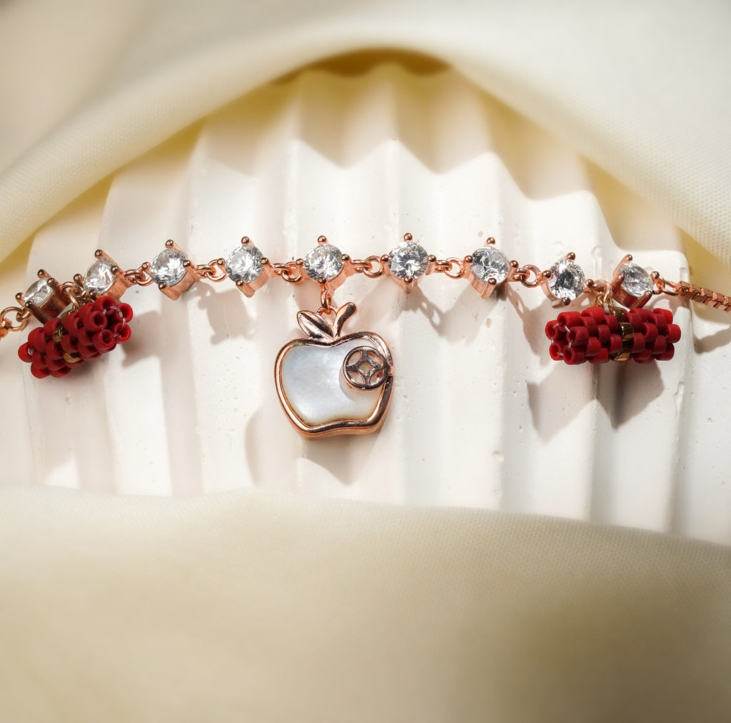 Close view of pearly white apple charm and red beaded barrels on a rose-gold crystal bracelet