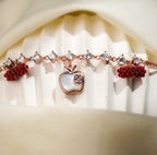 Close view of pearly white apple charm and red beaded barrels on a rose-gold crystal bracelet