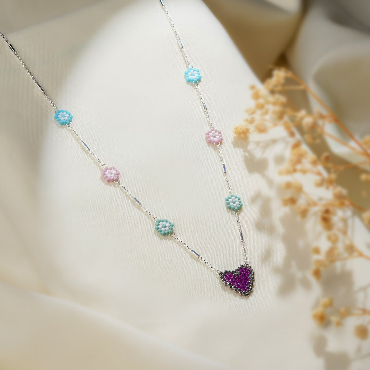 Silver bar-link necklace with turquoise, pink and mint beaded daisies and a purple heart on cream silk