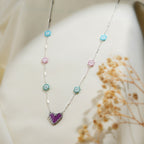 Close-up of pastel beaded daisies and silver-edged purple heart on silver bar-link chain